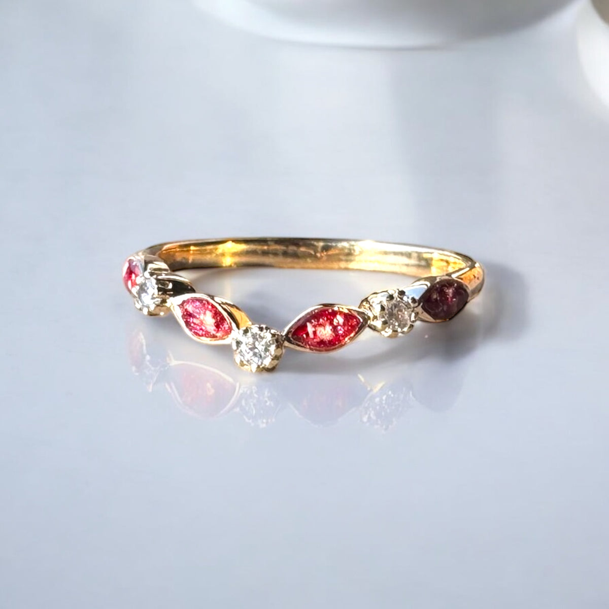 A 9K gold half eternity ring with a wishbone design, featuring red and clear crystals, with cremation ashes on a red resin stone