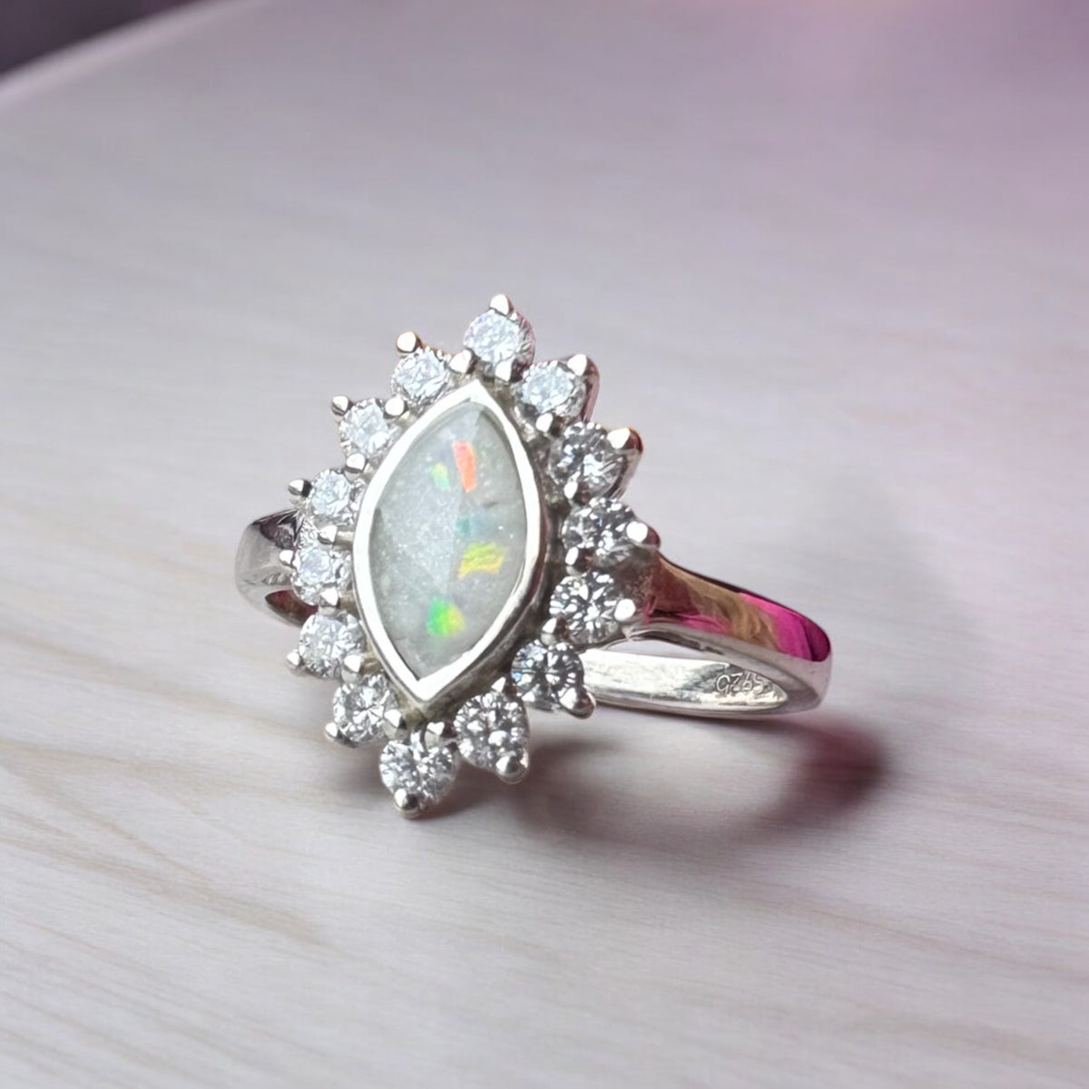 Angled view of a sterling silver marquise keepsake ring showing colourful opal flakes, breastmilk centre and surrounding cubic zirconia stones.